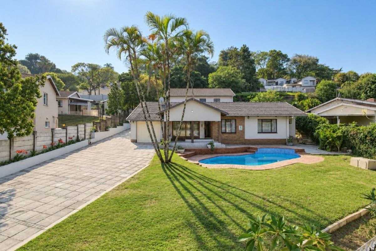 Rear view of the property featuring a swimming pool, paved driveway, landscaped garden, and a well-maintained brick and plaster house exterior.