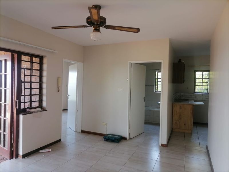 Open plan living area featuring tiled floors, a ceiling fan, and direct access to a functional kitchen and adjacent bathroom.