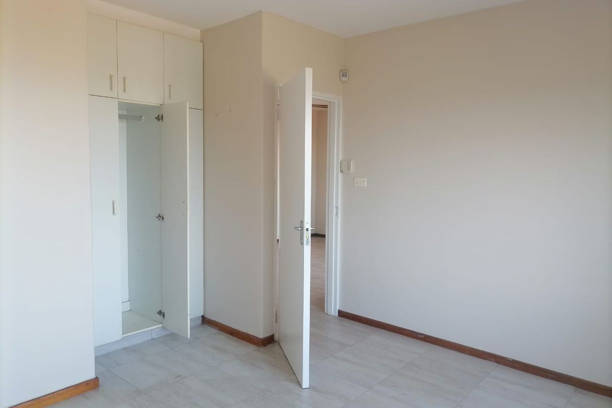 An empty bedroom featuring neutral wall paint, tiled flooring, and built-in storage cupboards.