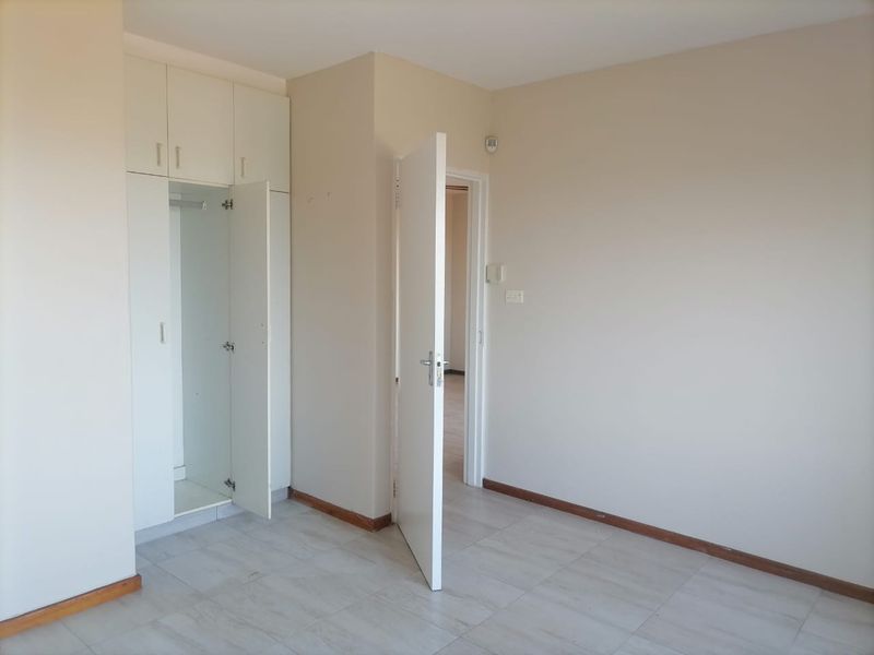 An empty bedroom featuring neutral wall paint, tiled flooring, and built-in storage cupboards.