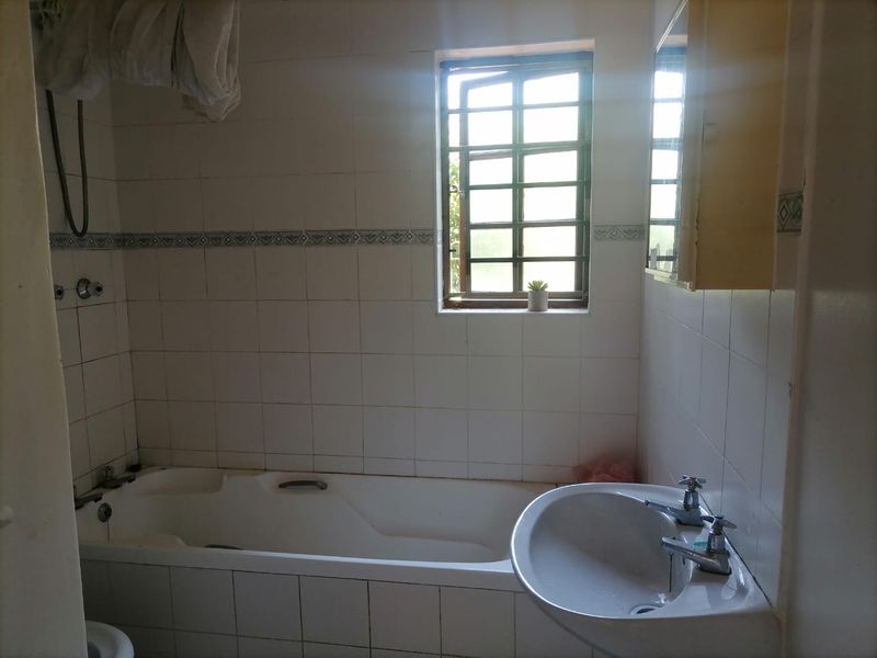 A dated bathroom featuring a standard bathtub, pedestal basin, and tiled walls, requiring modernization to improve its aesthetic and functional appeal.