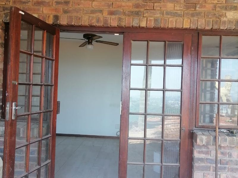 A covered patio area featuring exposed brickwork and timber-framed glass doors leading into an interior space with tiled flooring and a ceiling fan.