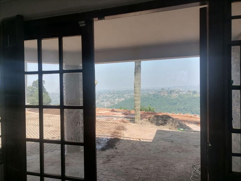 Covered patio area featuring timber-framed glass doors and paved flooring, offering expansive elevated views of the surrounding landscape.