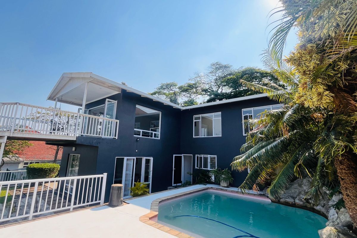 Rear exterior view of a multi-level home featuring a swimming pool, paved deck area, and an elevated balcony with white railings.
