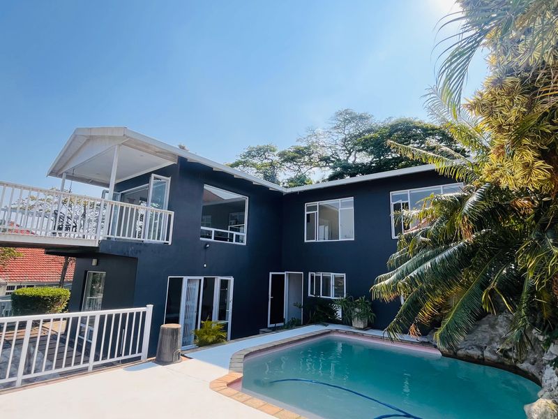 Rear exterior view of a multi-level home featuring a swimming pool, paved deck area, and an elevated balcony with white railings.
