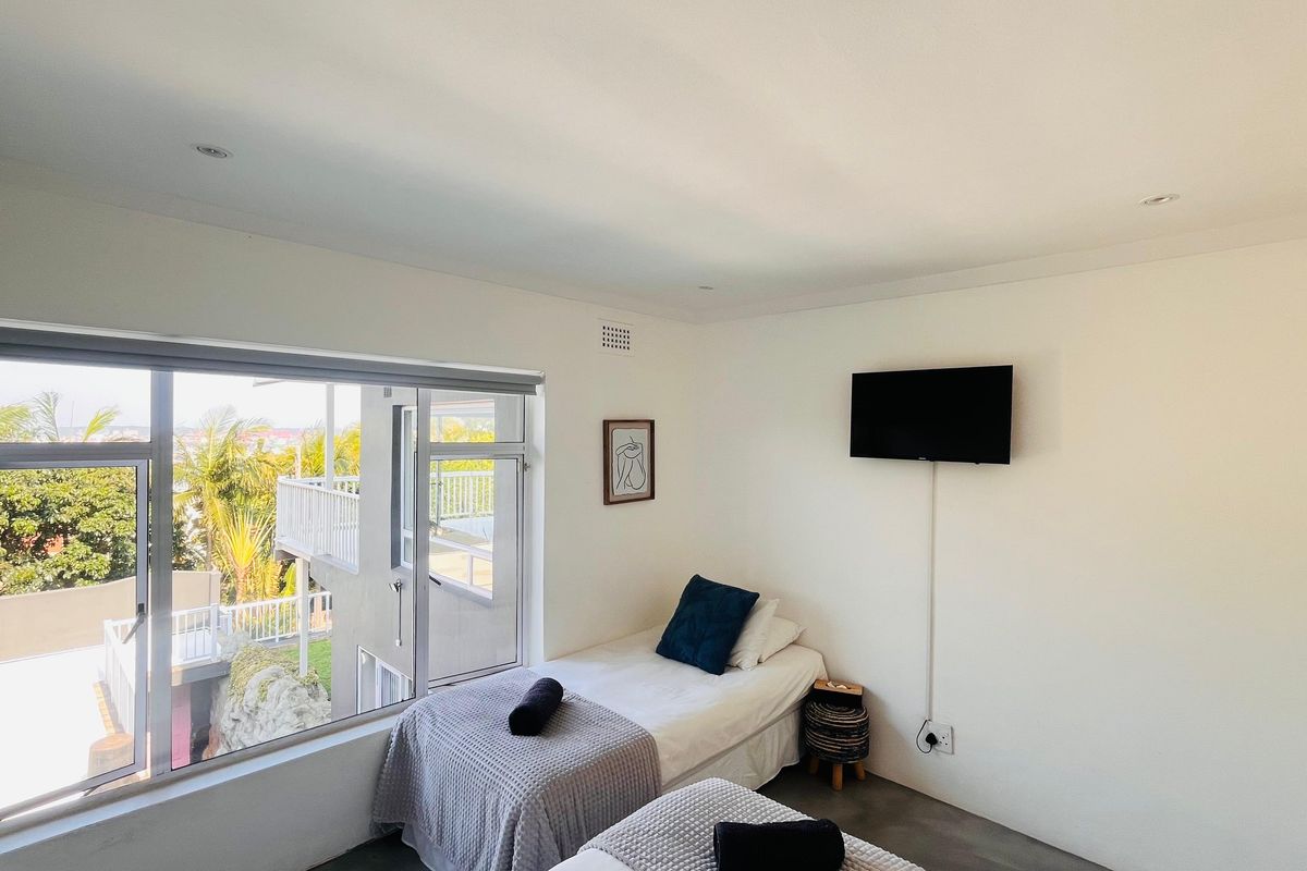 A bright bedroom featuring large aluminium-framed windows with garden views, recessed downlighting, and polished concrete flooring.