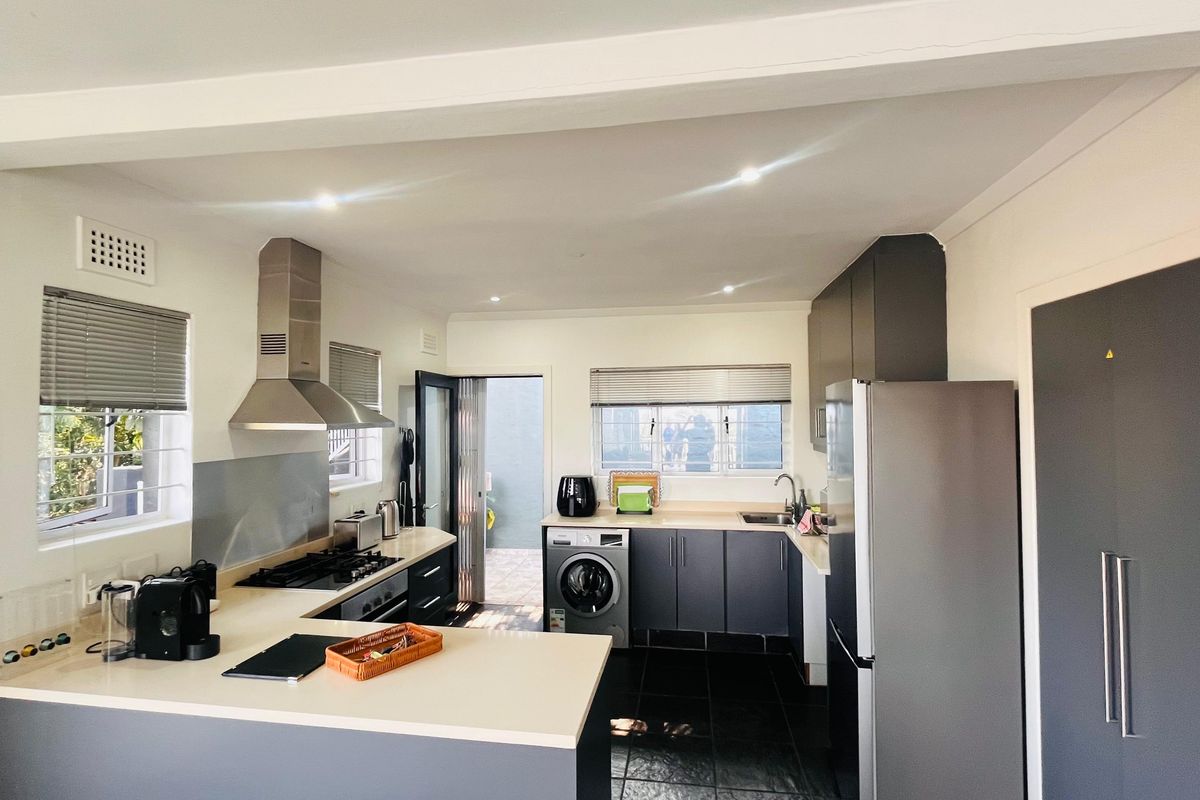 Modern kitchen featuring dark cabinetry, stone countertops, gas hob, stainless steel extractor, and integrated laundry space with direct access to the exterior.