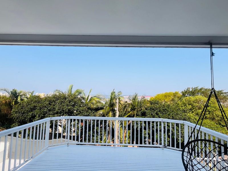 A covered balcony featuring white timber decking and a matching balustrade, offering an elevated outdoor space with scenic treetop views.