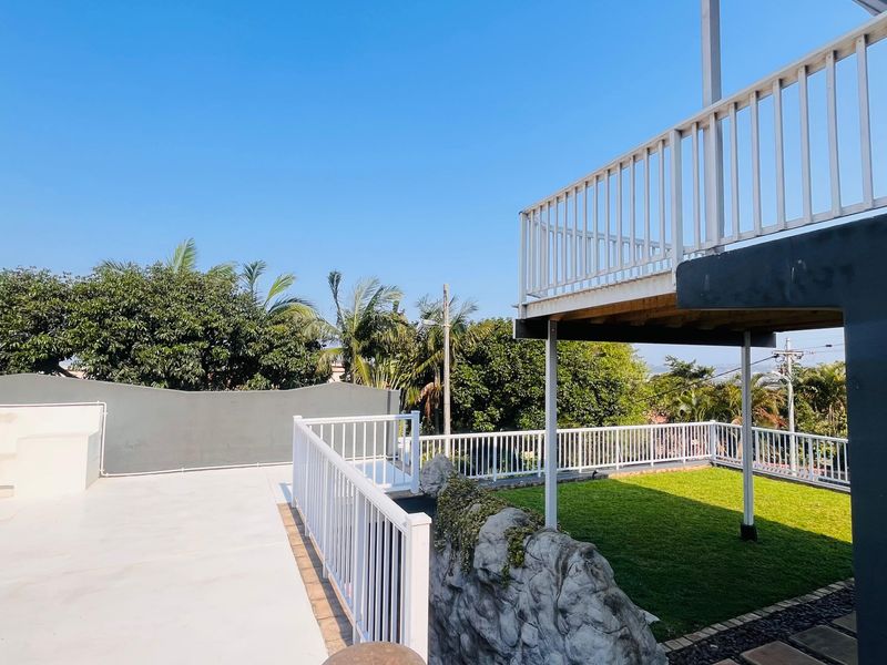 An elevated outdoor deck area featuring a white metal balustrade, artificial grass section, and decorative rock landscaping, providing a clean and modern outdoor space.