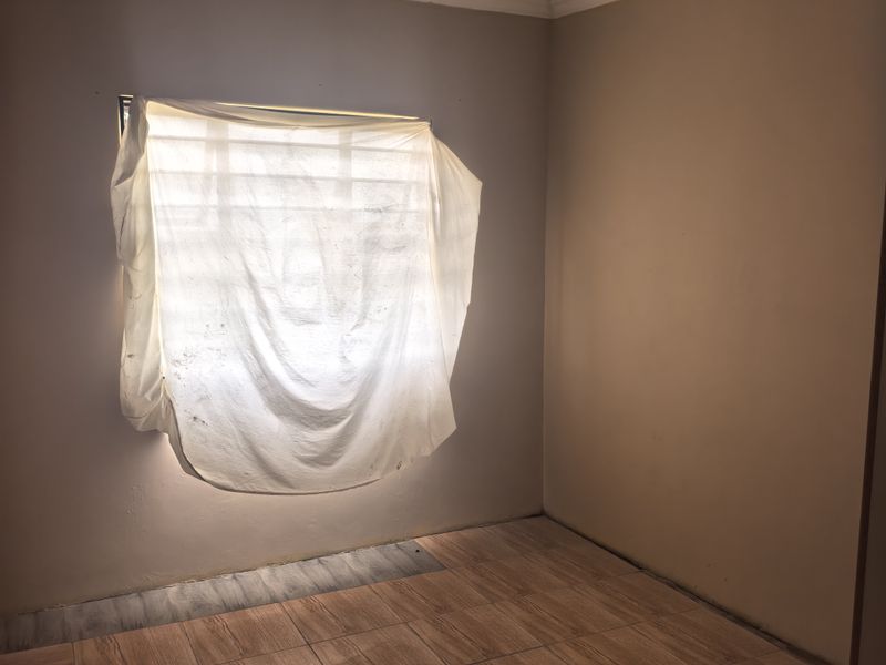 An empty bedroom featuring wood-look tiled flooring, security bars on the window, and a coved ceiling, awaiting finishing touches.
