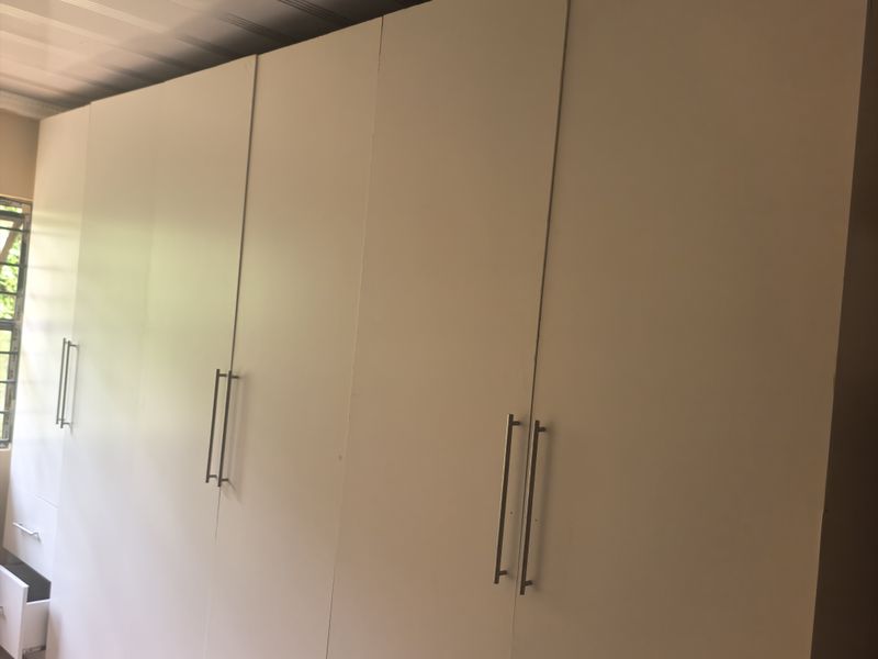 A bedroom featuring extensive built-in white cabinetry, tiled flooring, and a suspended ceiling. The space is currently vacant and ready for personalization.