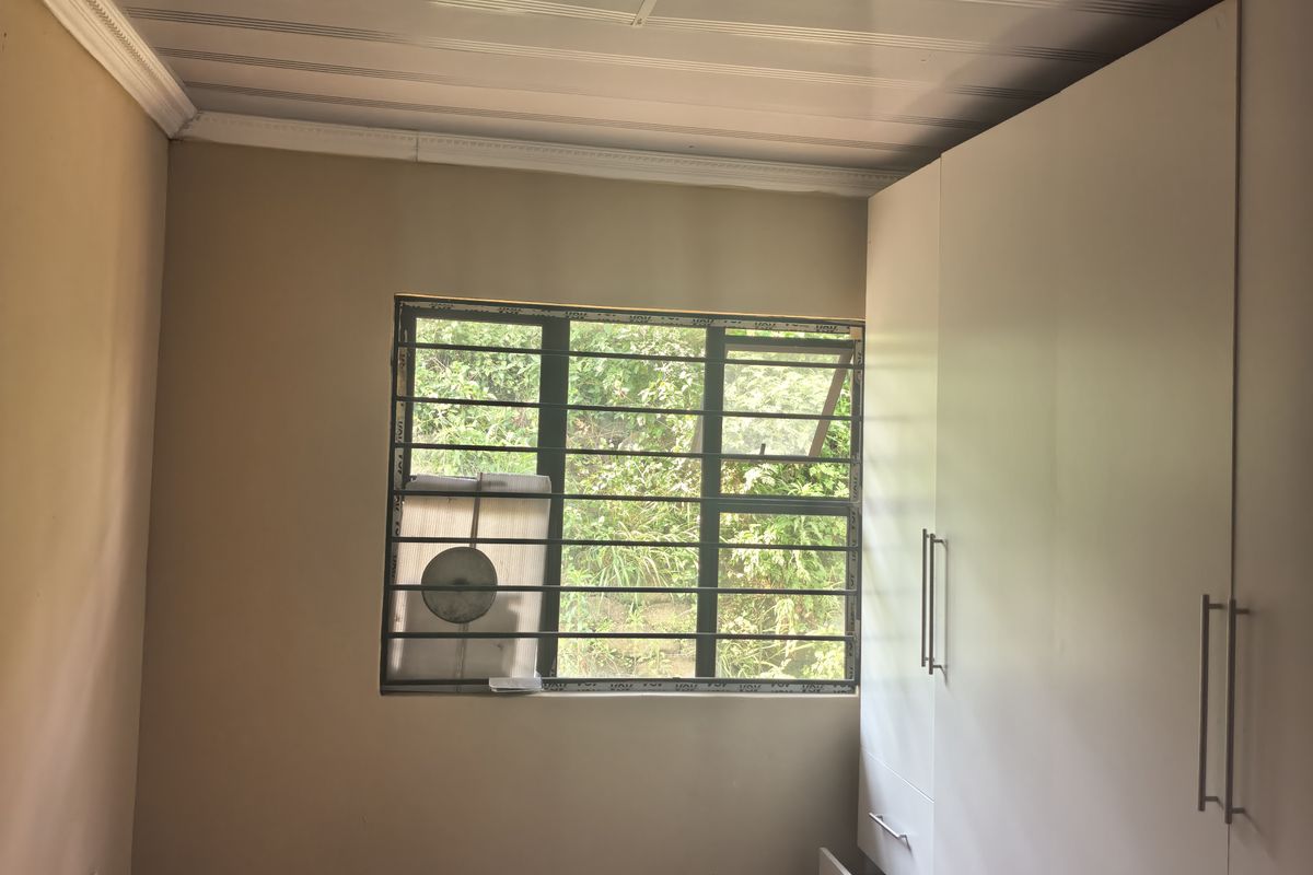 A bedroom featuring built-in cupboards, tiled flooring, and security bars on the window. The room is currently vacant and ready for personalization.