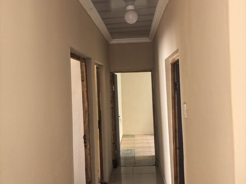 A narrow hallway featuring tiled flooring and a panelled ceiling, currently showing unfinished door frames and exposed wall edges requiring completion.