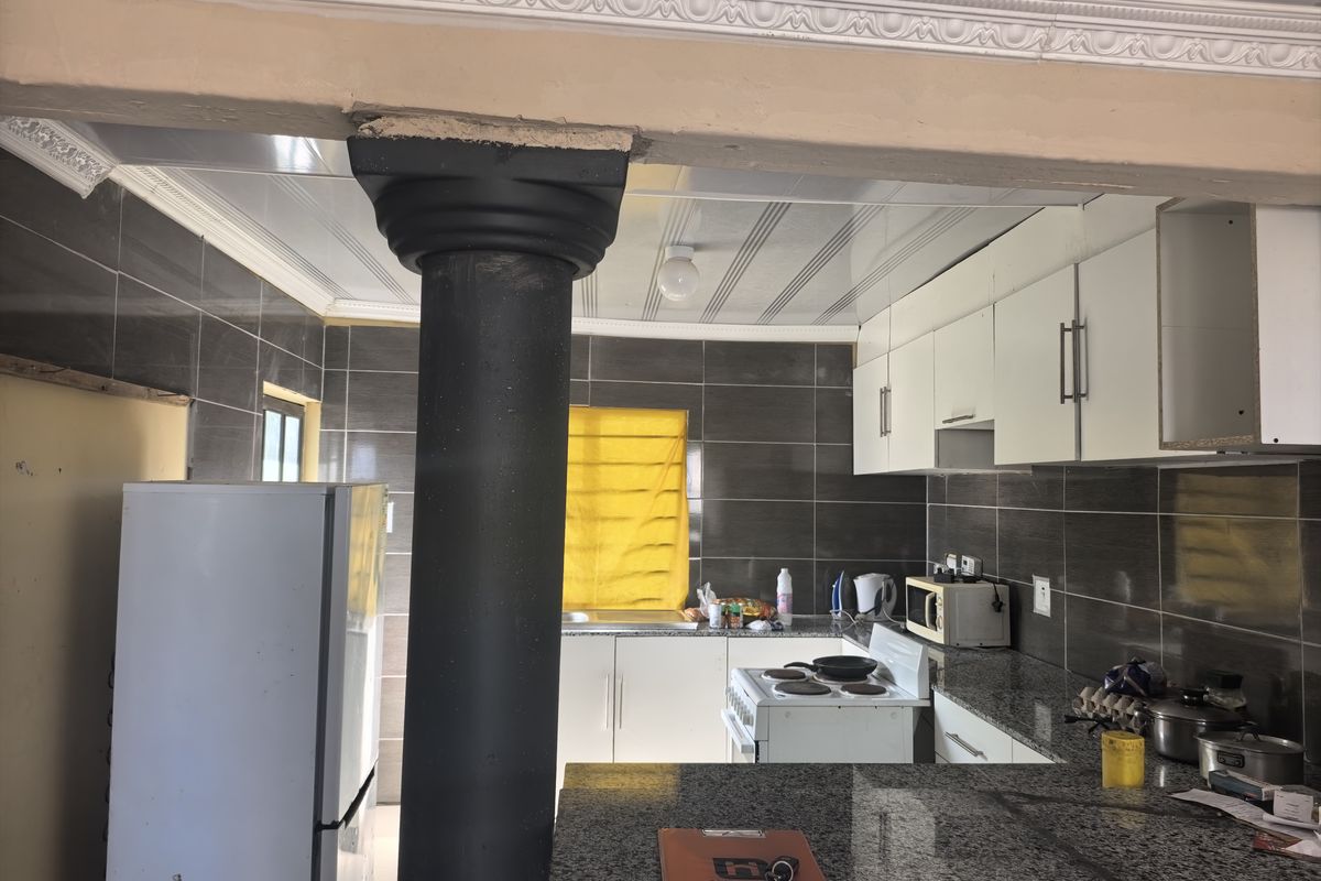 A functional kitchen featuring granite countertops, dark tiled walls, and white cabinetry, with a prominent structural column separating the space.