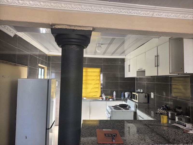 A functional kitchen featuring granite countertops, dark tiled walls, and white cabinetry, with a prominent structural column separating the space.