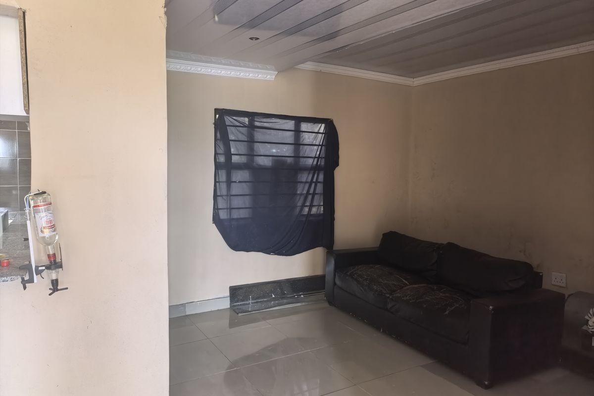 A living area featuring tiled flooring, coved ceilings with plastic paneling, and a window with security bars, showing signs of wear on the walls.