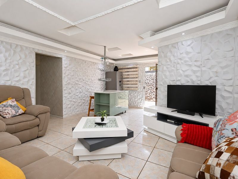 Open-plan living area featuring textured 3D wall panels, decorative ceiling molding, ceramic tile flooring, and a central kitchen island with integrated lighting.