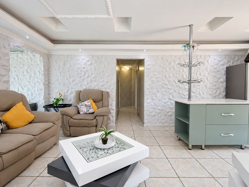 A modern living area featuring decorative 3D wall panels, recessed ceiling lighting, and tiled flooring, creating a bright and contemporary open-plan space.