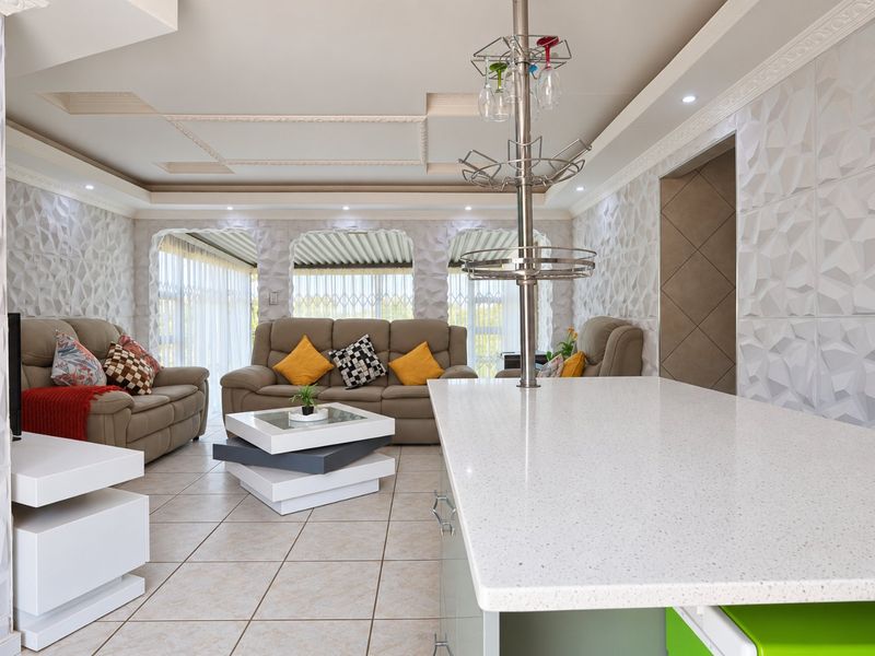 Modern open-plan living area featuring a quartz-topped kitchen island, distinctive 3D textured wall panels, and a sophisticated recessed ceiling design with integrated lighting.