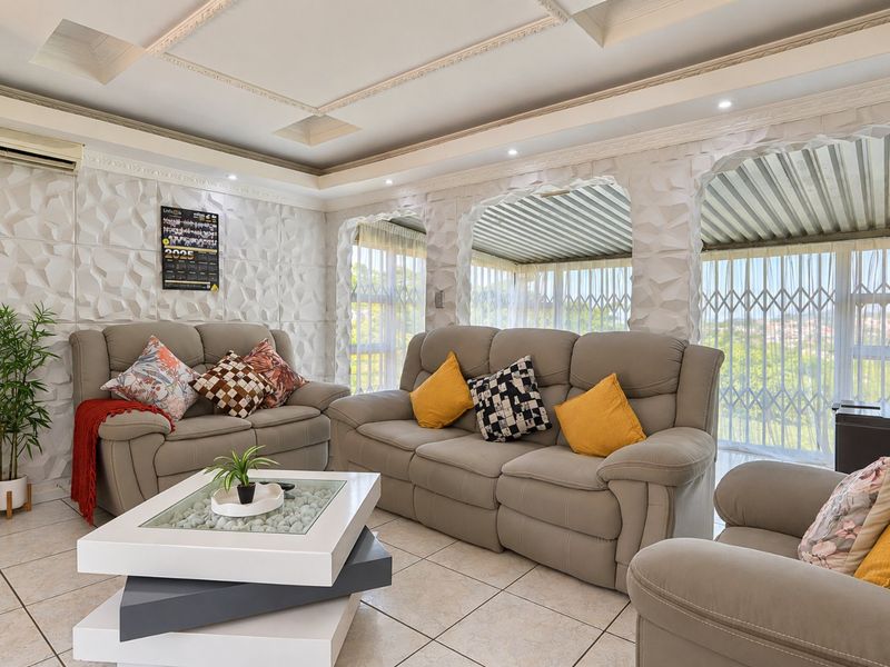 A well-maintained living room featuring textured wall panels, a decorative coffered ceiling with recessed lighting, and tiled flooring.