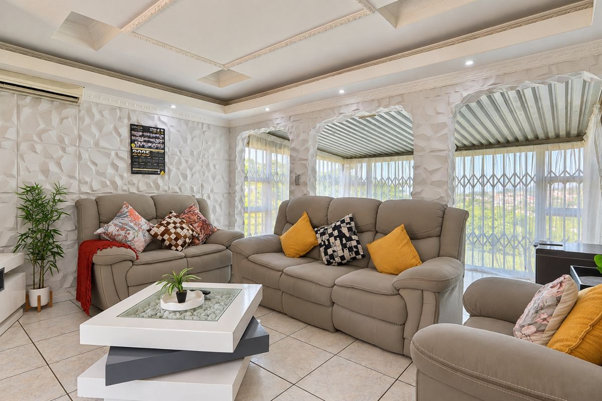 A well-maintained living room featuring textured wall panels, a decorative coffered ceiling with recessed lighting, and tiled flooring.