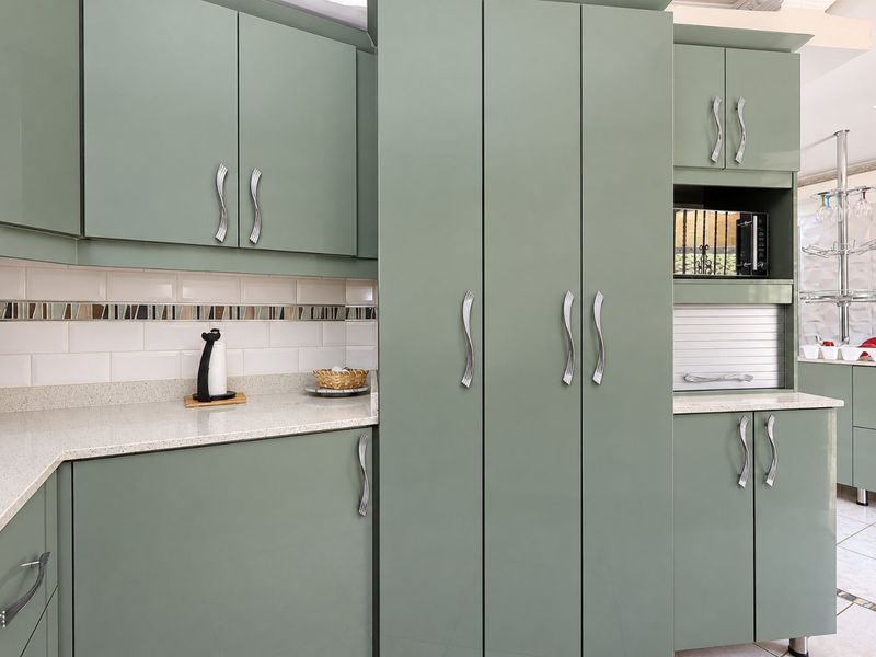 Modern kitchen featuring sage green cabinetry, stone countertops, and a decorative subway tile backsplash with integrated appliance storage.