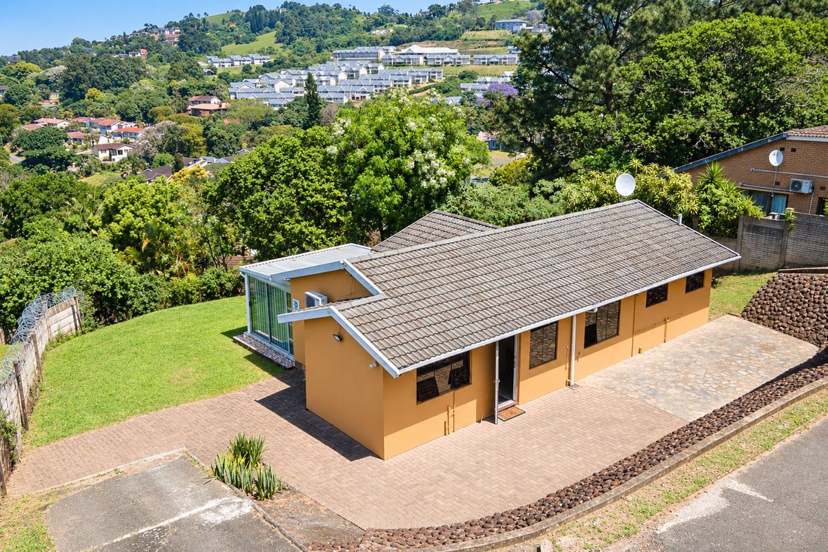 Aerial view of a residential property featuring a tiled roof, paved driveway, and surrounding landscaped garden with scenic hillside views.