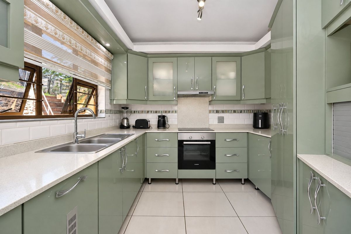 A well-maintained kitchen featuring sage green cabinetry, stone countertops, a subway tile backsplash, and integrated stainless steel appliances.