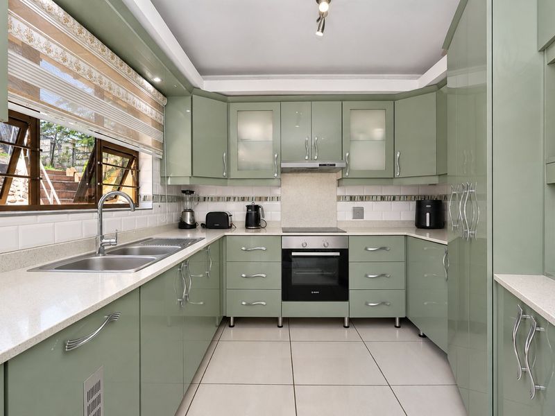 A well-maintained kitchen featuring sage green cabinetry, stone countertops, a subway tile backsplash, and integrated stainless steel appliances.