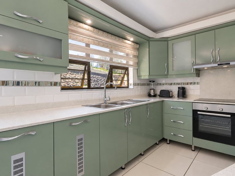 Modern kitchen featuring sage green cabinetry, stone-look countertops, integrated stainless steel appliances, and a tiled backsplash with recessed lighting.