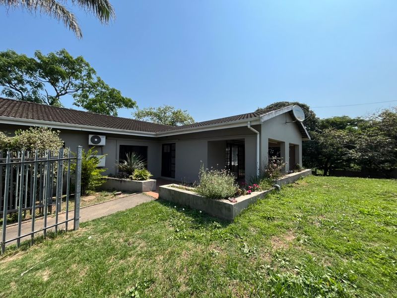 Front exterior view of a single-story house featuring a tiled roof, concrete planter boxes, and metal security fencing in a garden setting.