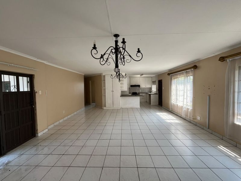 Spacious open-plan living and kitchen area featuring tiled flooring, built-in cabinetry, and a central chandelier, offering a blank canvas for renovation.