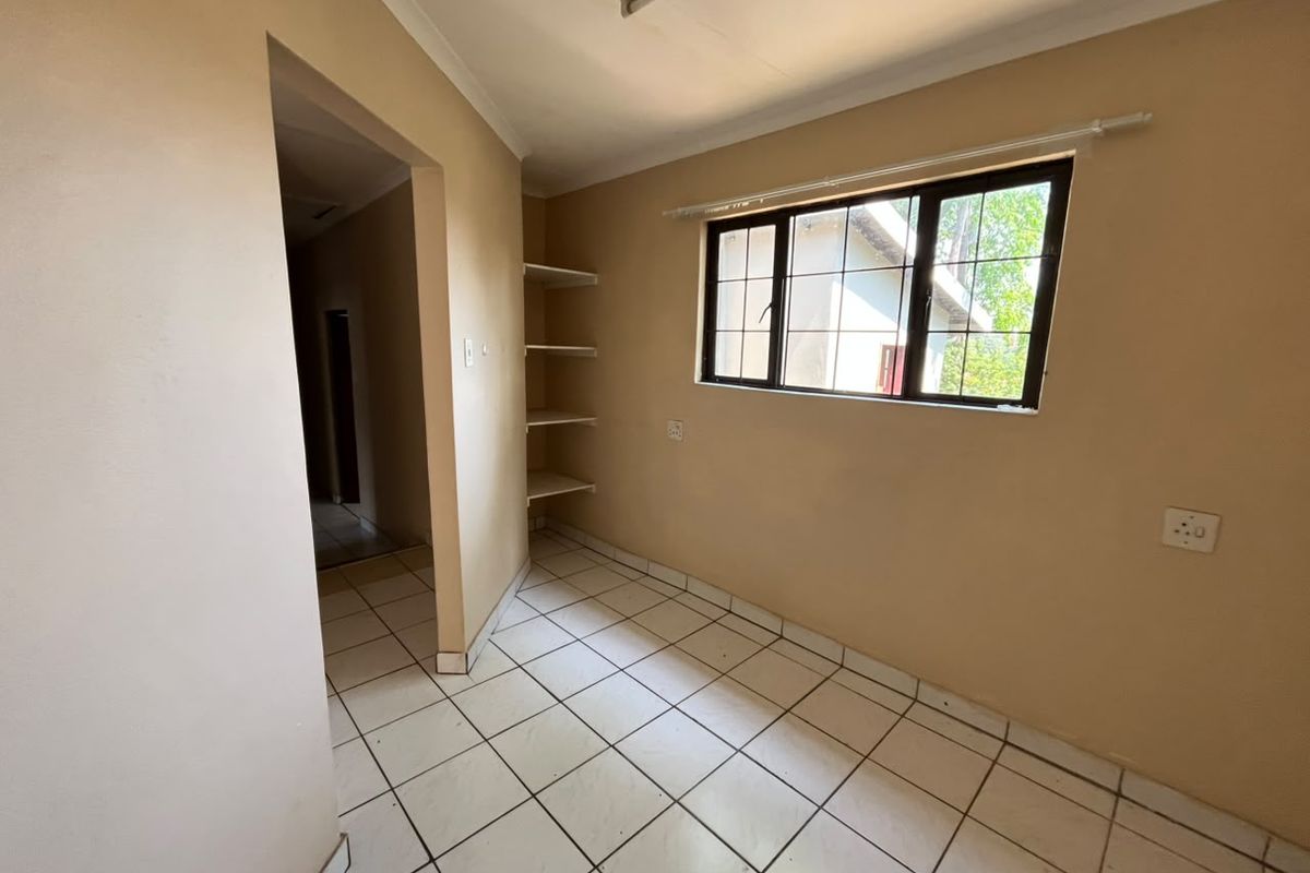 An empty bedroom featuring tiled flooring, built-in shelving, and a window with security bars, offering a blank canvas for renovation.