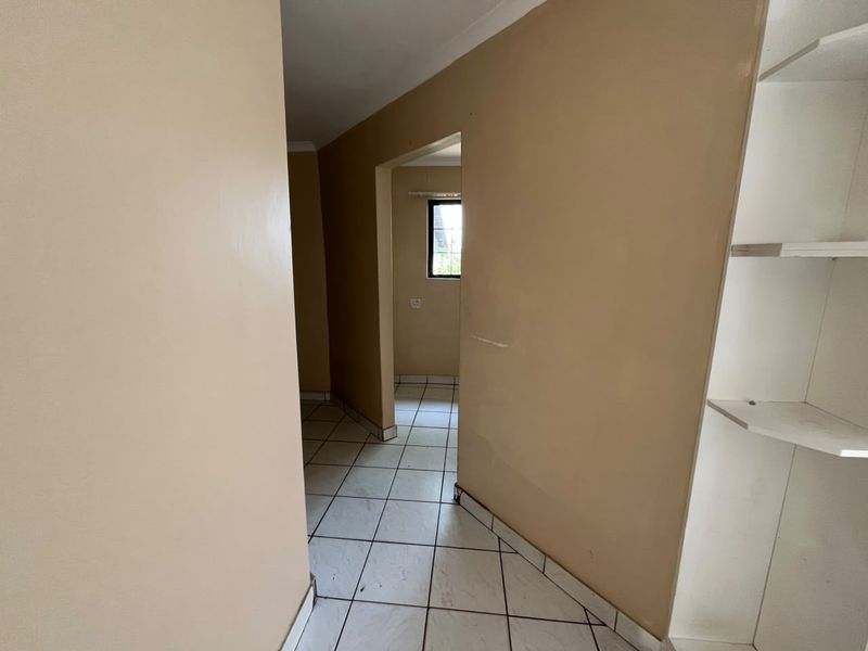 A vacant hallway featuring tiled flooring and built-in shelving, leading into an adjacent room with a window.
