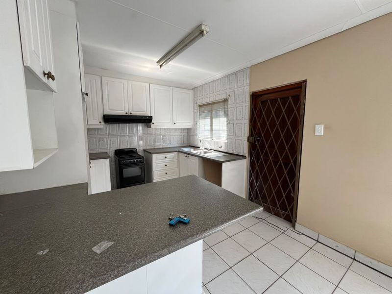 A functional kitchen featuring white cabinetry, laminate countertops, a freestanding stove, and tiled flooring, offering a clean canvas for potential modern updates.