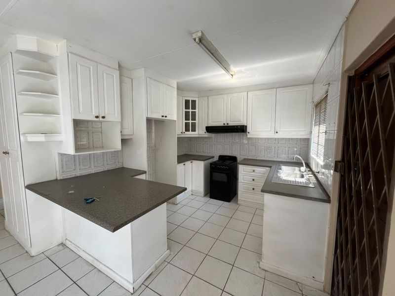 A functional kitchen featuring white cabinetry, laminate countertops, a stainless steel sink, and a freestanding stove with an extractor fan.