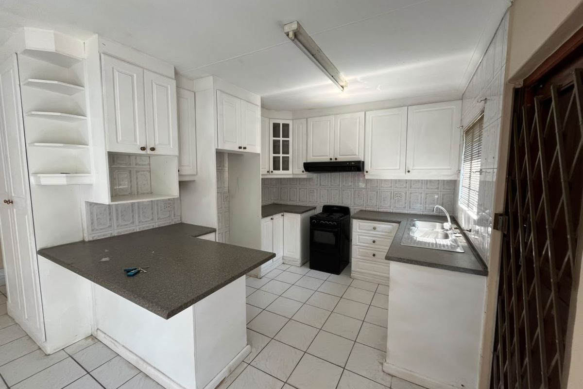 A functional kitchen featuring white cabinetry, laminate countertops, a stainless steel sink, and a freestanding stove with an extractor fan.