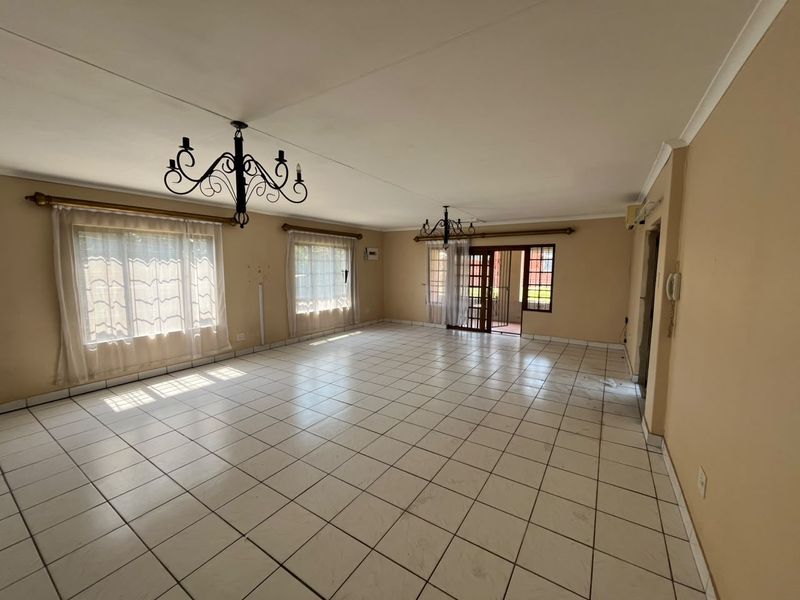 Spacious, light-filled living area featuring neutral tiled flooring, classic wrought iron chandeliers, and direct access to an outdoor patio through sliding glass doors.