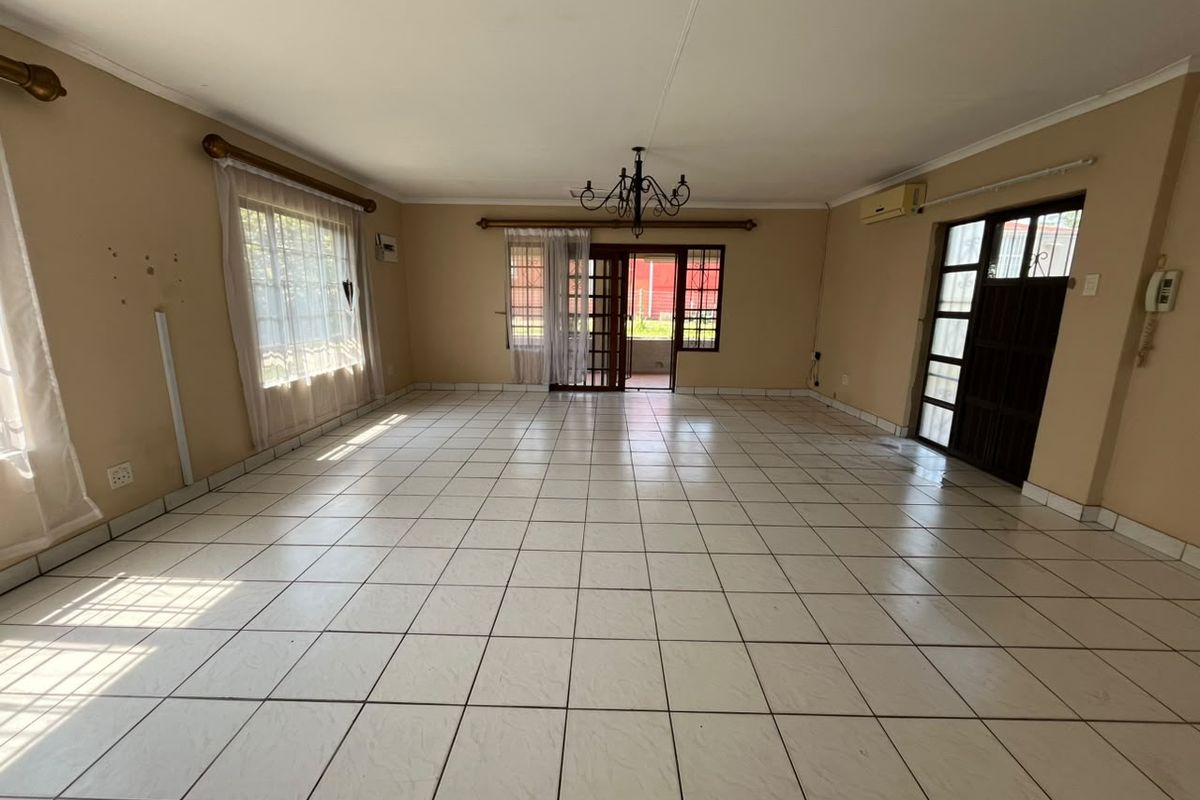Spacious, empty living area featuring neutral tiled flooring, a central chandelier, and direct access to the exterior through a sliding glass door.