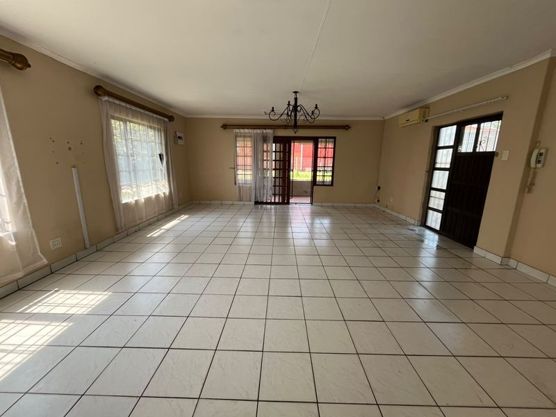 Spacious, empty living area featuring neutral tiled flooring, a central chandelier, and direct access to the exterior through a sliding glass door.