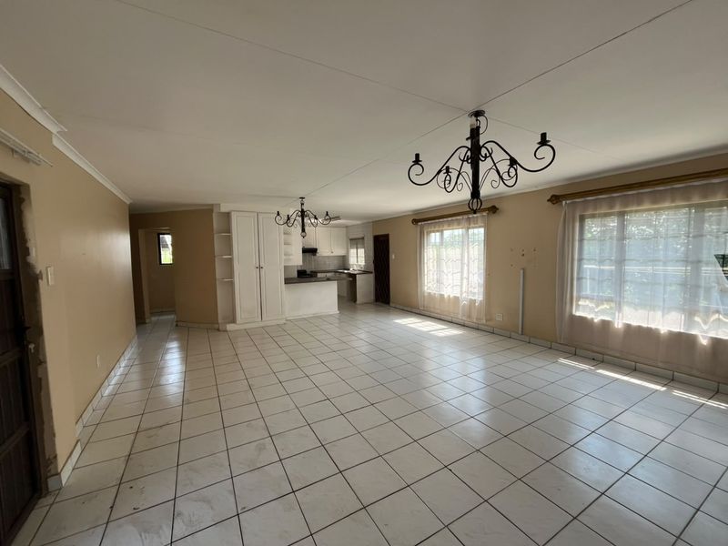 Spacious open-plan living and kitchen area featuring tiled flooring, built-in cabinetry, and ample natural light, offering a blank canvas for renovation.