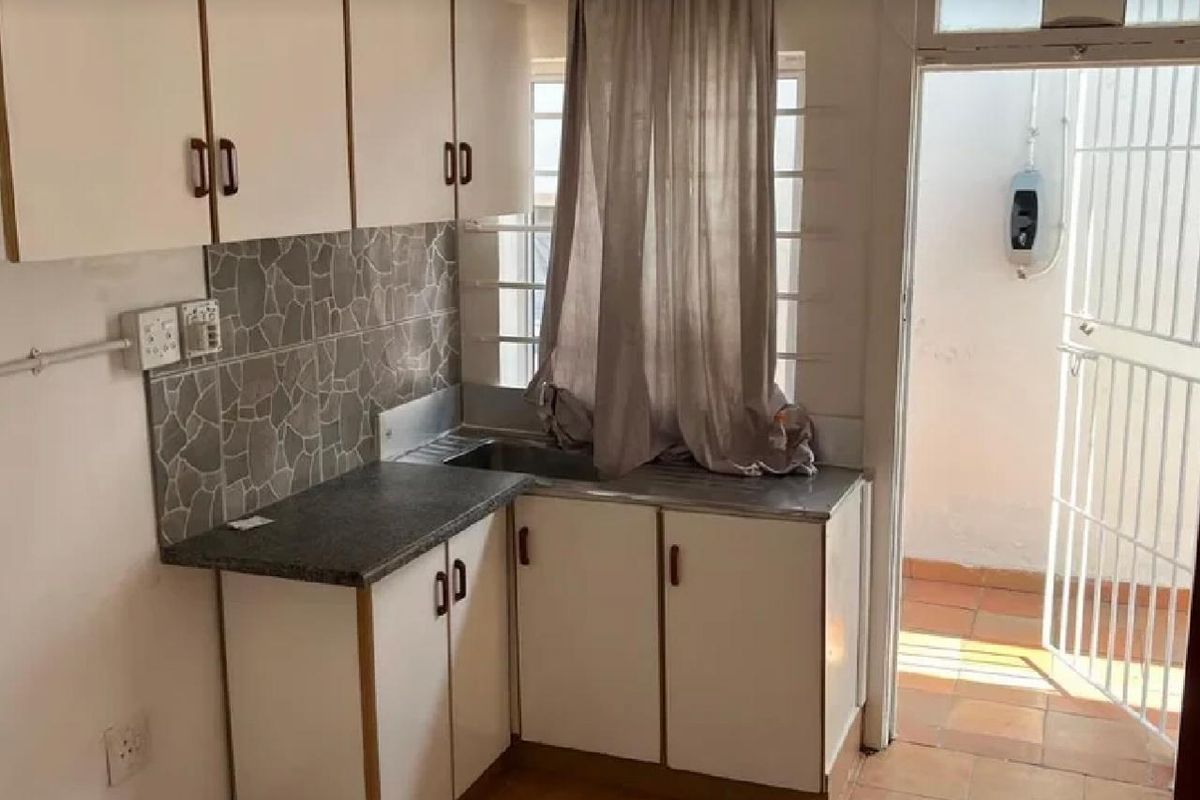 A compact kitchen featuring white built-in cabinetry, stone-look tile backsplash, and direct access to an outdoor area through a security gate.