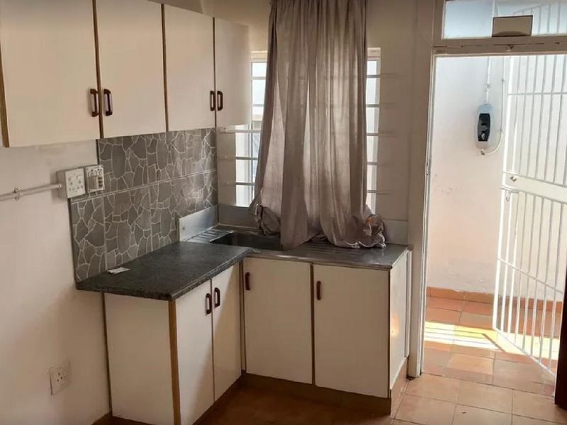 A compact kitchen featuring white built-in cabinetry, stone-look tile backsplash, and direct access to an outdoor area through a security gate.