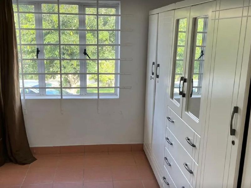 A bedroom featuring tiled flooring, a large built-in wardrobe with mirrored panels, and a window fitted with security bars.