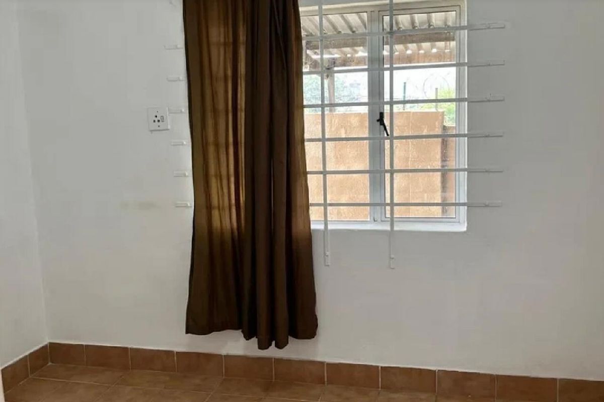An empty bedroom featuring tiled flooring, a window with security bars, and plain white walls.