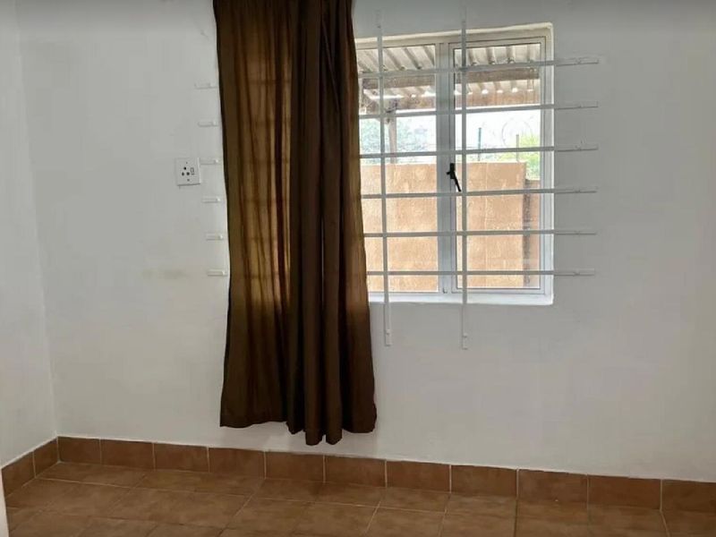 An empty bedroom featuring tiled flooring, a window with security bars, and plain white walls.