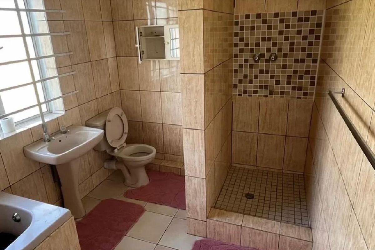 A functional bathroom featuring a pedestal basin, toilet, and a walk-in shower with mosaic tile accents and full-height wall tiling.