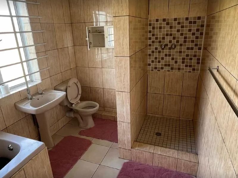 A functional bathroom featuring a pedestal basin, toilet, and a walk-in shower with mosaic tile accents and full-height wall tiling.