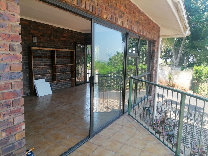 A spacious covered patio featuring exposed brick walls, tiled flooring, and a metal balustrade, offering a seamless transition to the outdoor area.
