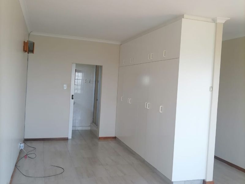A bright, empty bedroom featuring neutral tiled flooring, ample built-in cupboard storage, and a doorway leading to an en-suite bathroom.